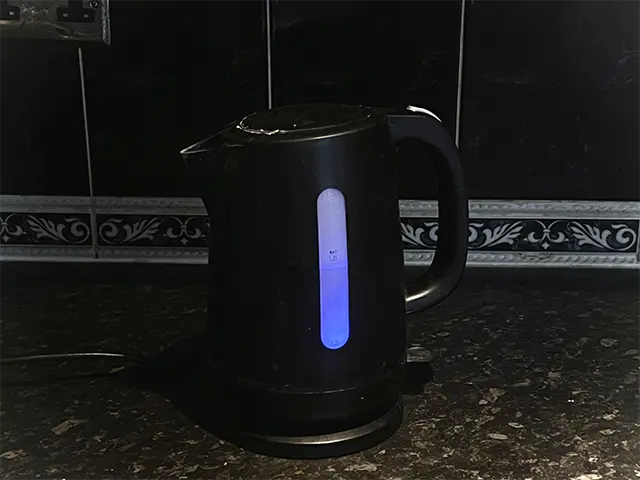Electric kettle glowing blue on its circular base in a dim kitchen.
